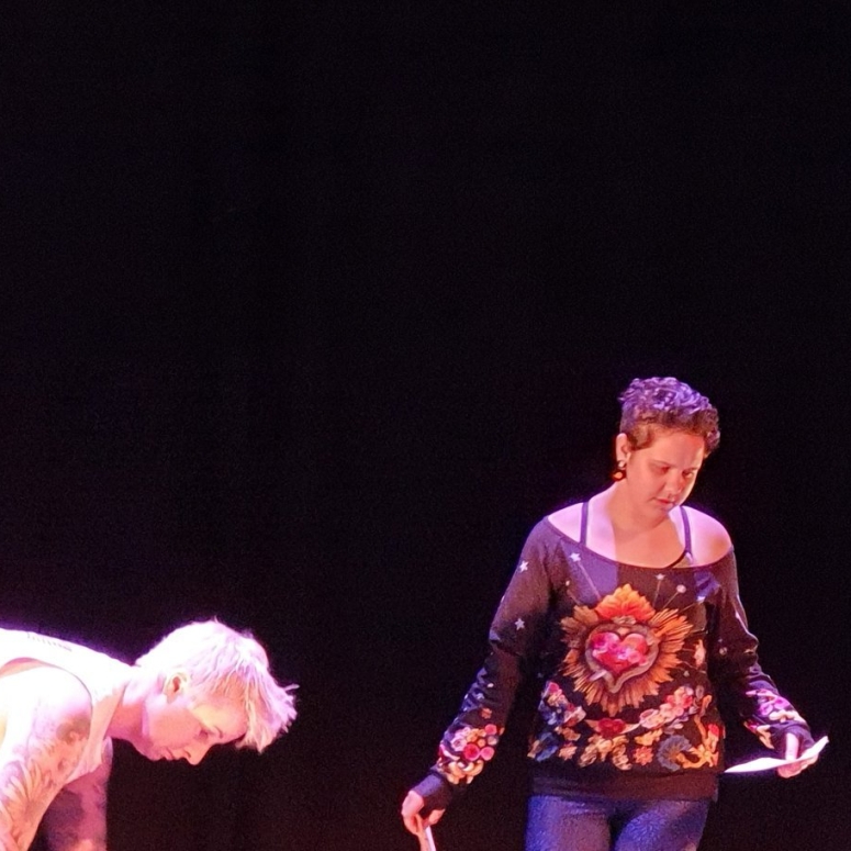 Four people moving on a stage, picking up pieces of paper.
